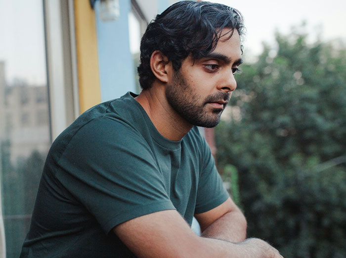 Man in a green shirt looks thoughtful, leaning on a balcony, with trees in the background. Man in a green shirt looks thoughtful, leaning on a balcony, with trees in the background.