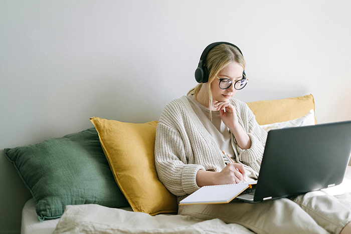 Woman in headphones sitting on a bed with a laptop, taking notes related to a hookup after a long relationship. Woman in headphones sitting on a bed with a laptop, taking notes related to a hookup after a long relationship.