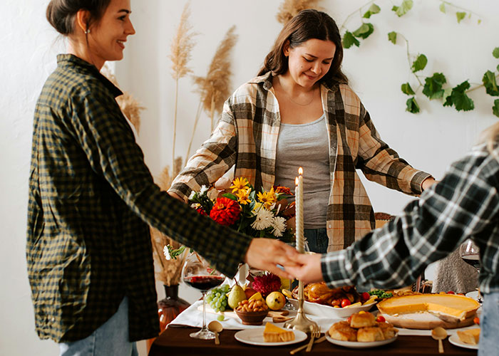 Women smiling and holding hands around a Thanksgiving table with flowers and dishes. Women smiling and holding hands around a Thanksgiving table with flowers and dishes.