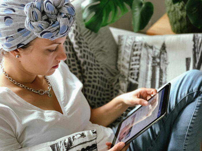 Woman reading on a tablet, seated on a couch with themed pillows, contemplating her daughter's exotic trip. Woman reading on a tablet, seated on a couch with themed pillows, contemplating her daughter's exotic trip.