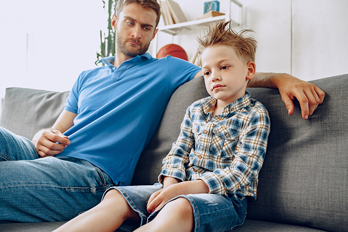 Man in blue polo looks concerned while sitting beside a boy on a sofa, reflecting tension in a family relationship. Man in blue polo looks concerned while sitting beside a boy on a sofa, reflecting tension in a family relationship.