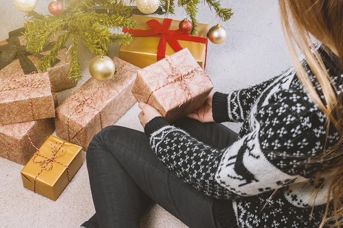 Woman in festive sweater holding gift near a Christmas tree with multiple presents. Woman in festive sweater holding gift near a Christmas tree with multiple presents.