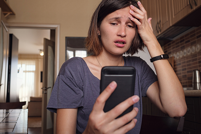 Woman looking upset while reading a message on her phone, testing the impact of calling her by a mean name. Woman looking upset while reading a message on her phone, testing the impact of calling her by a mean name.