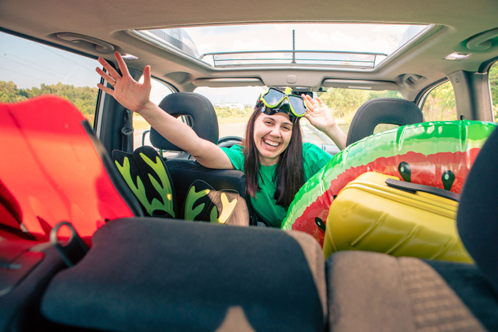 Woman happily packing car with vacation gear, waving from backseat. Woman happily packing car with vacation gear, waving from backseat.