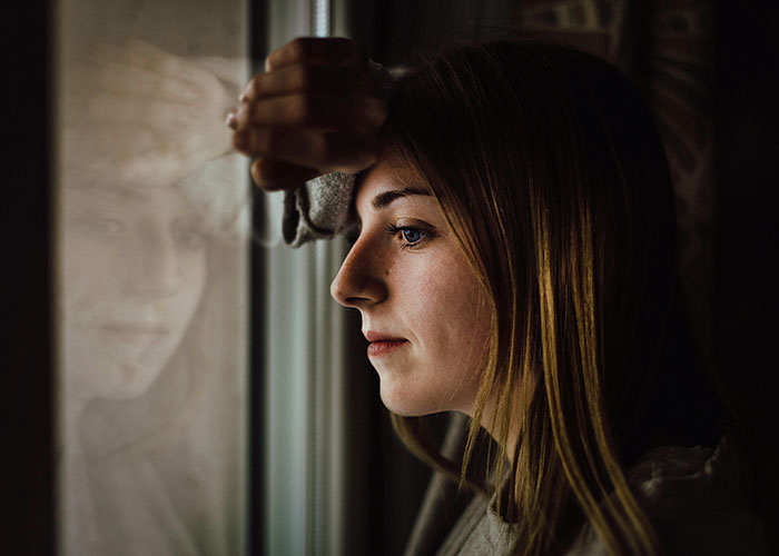Woman looking out window, feeling conflicted over financial and family decisions. Woman looking out window, feeling conflicted over financial and family decisions.