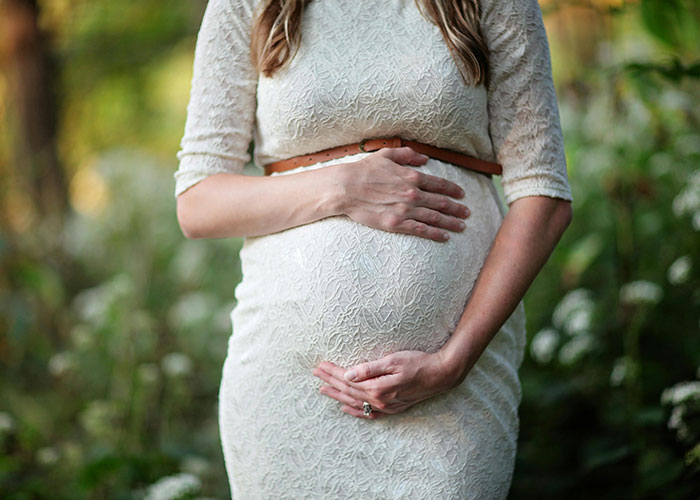 Pregnant woman in lace dress standing in garden, hands on her belly, serene and thoughtful. Pregnant woman in lace dress standing in garden, hands on her belly, serene and thoughtful.