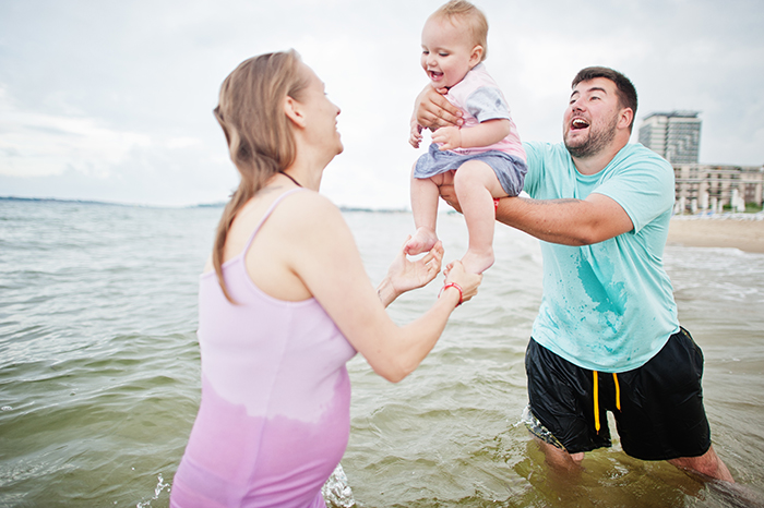 Family enjoying vacation at the beach, playing in the water with a baby. Family enjoying vacation at the beach, playing in the water with a baby.
