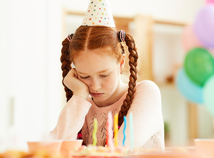 Girl wearing party hat, looking upset at a birthday table. Girl wearing party hat, looking upset at a birthday table.