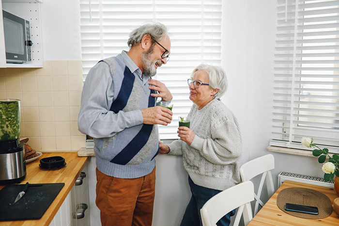 Elderly couple in a kitchen, smiling and holding drinks, representing in-laws visiting unexpectedly on vacation. Elderly couple in a kitchen, smiling and holding drinks, representing in-laws visiting unexpectedly on vacation.