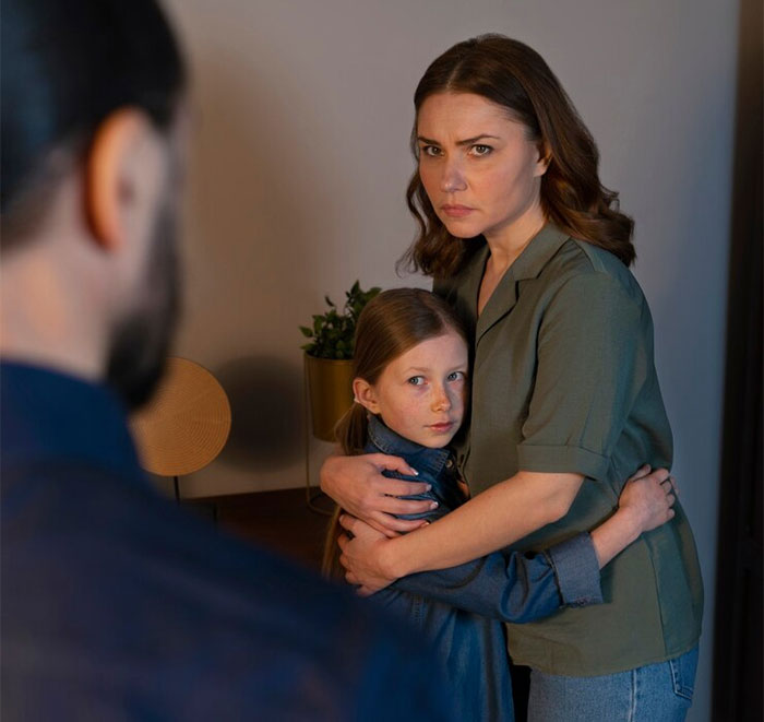 Woman looking upset, hugging a child, with a man in the foreground. Woman looking upset, hugging a child, with a man in the foreground.