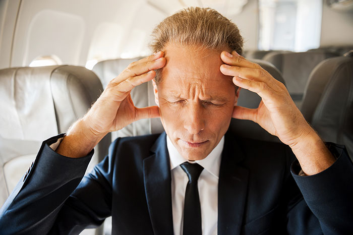 Frustrated passenger in a suit with hands on temples, seated on a plane. Frustrated passenger in a suit with hands on temples, seated on a plane.