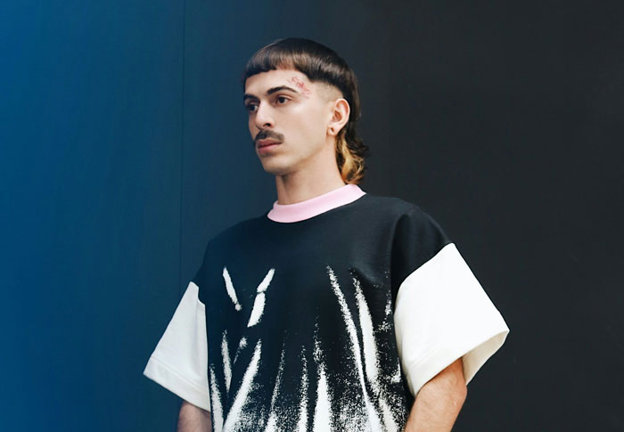 Person in bold fashion trend with unique hairstyle and graphic shirt, expressing a disliked style.