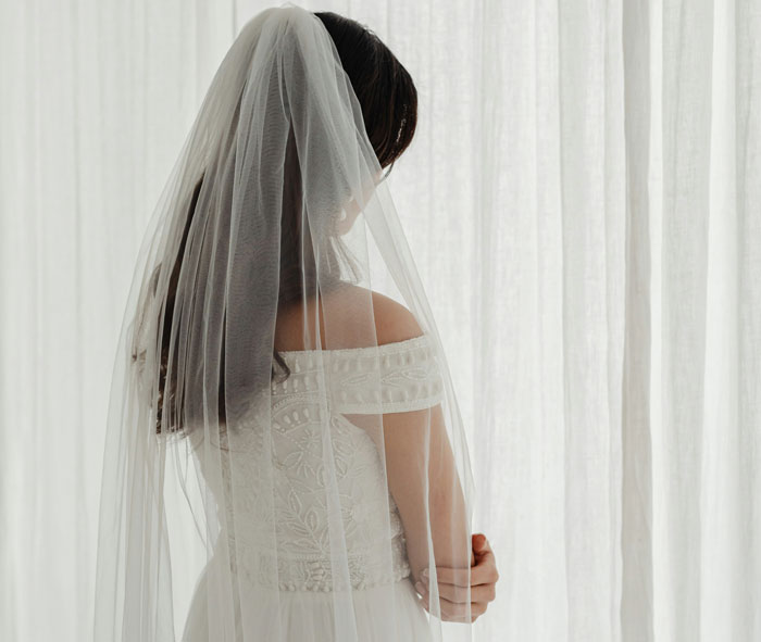 Bride in veil and $7,000 dream dress standing by curtains, reflecting on a vanished gown incident. Bride in veil and $7,000 dream dress standing by curtains, reflecting on a vanished gown incident.