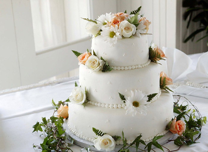 Three-tier wedding cake with floral decoration on a white tablecloth. Three-tier wedding cake with floral decoration on a white tablecloth.