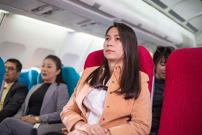 Passenger on a plane looks upset, sitting upright in her red seat, surrounded by other travelers, related to seat denial incident. Passenger on a plane looks upset, sitting upright in her red seat, surrounded by other travelers, related to seat denial incident.