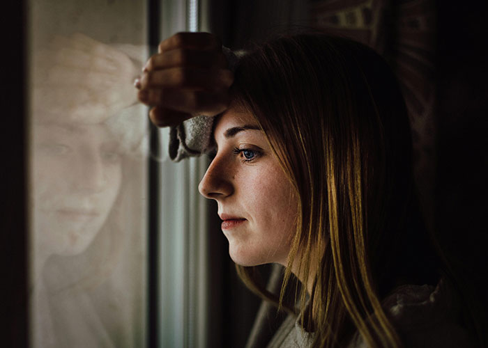 Woman looks out window thoughtfully, reflecting on secret discovered by roommates, changing everything. Woman looks out window thoughtfully, reflecting on secret discovered by roommates, changing everything.