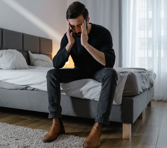 A man sits on a bed appearing distressed, wearing a black sweater and jeans, highlighting family tension and divorce issues. A man sits on a bed appearing distressed, wearing a black sweater and jeans, highlighting family tension and divorce issues.