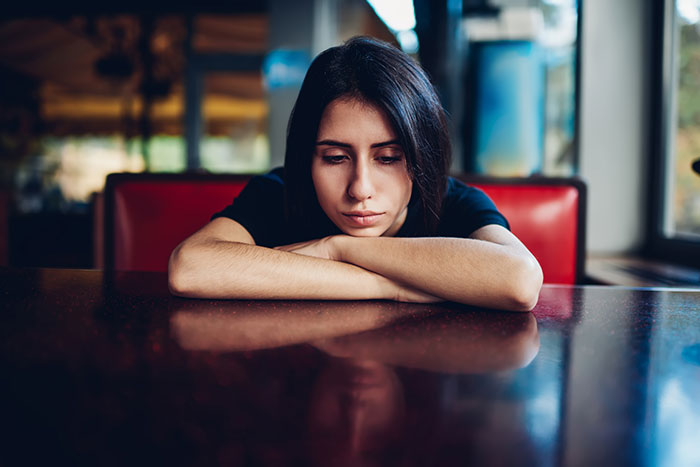Woman reflecting on boyfriend's behavior, seated at a table and appearing thoughtful and concerned. Woman reflecting on boyfriend's behavior, seated at a table and appearing thoughtful and concerned.