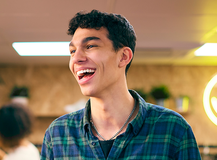 Teenager laughing in a warm-lit room, wearing a plaid shirt. Teenager laughing in a warm-lit room, wearing a plaid shirt.