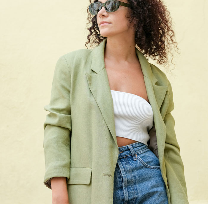 Woman wearing a green blazer, white top, and jeans, depicting a controversial fashion trend in current discussions.