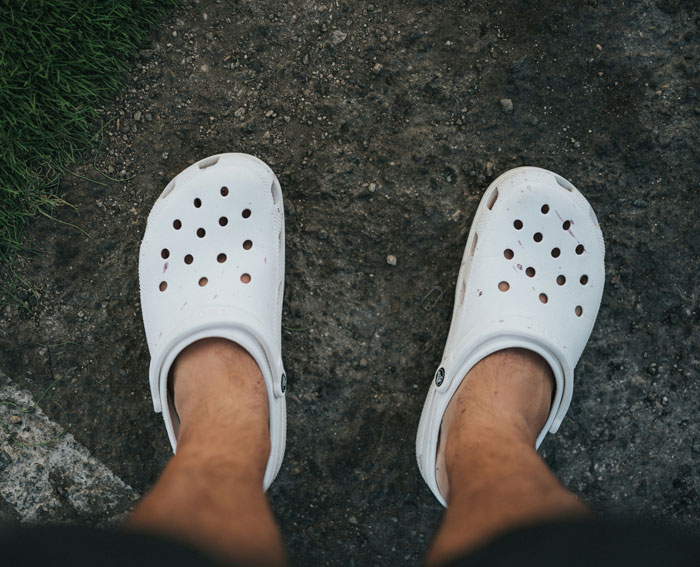 Worn white Crocs on a person’s feet, showcasing a fashion trend some people dislike.