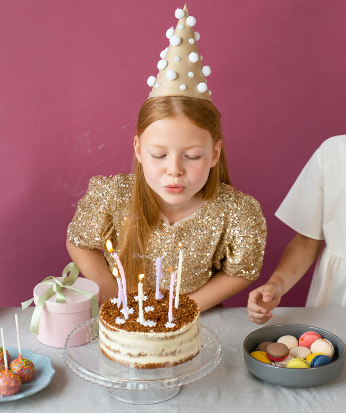 Girl in a party hat blowing out candles on a cake during a birthday celebration. Girl in a party hat blowing out candles on a cake during a birthday celebration.