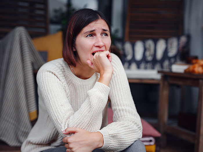A woman looking upset in a cozy, indoor setting, wearing a white sweater, with home decor in the background. A woman looking upset in a cozy, indoor setting, wearing a white sweater, with home decor in the background.