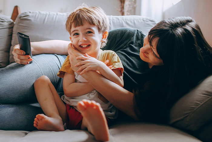 A woman comforts a smiling toddler with a remote, highlighting themes of toddler concussion care. A woman comforts a smiling toddler with a remote, highlighting themes of toddler concussion care.