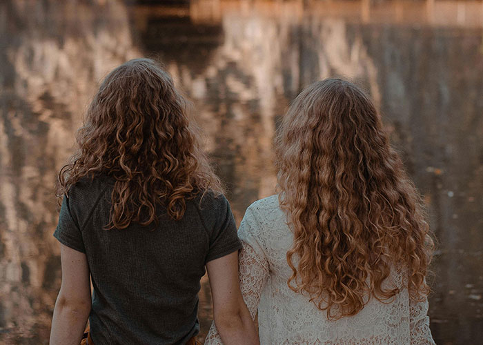Two women with curly hair sit by a serene lake, highlighting financial choices and family dynamics. Two women with curly hair sit by a serene lake, highlighting financial choices and family dynamics.