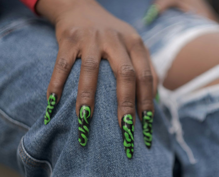 Close-up of a hand with green leopard print nails resting on ripped jeans, reflecting fashion trends.
