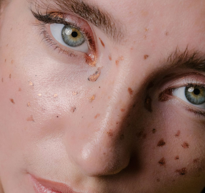 Close-up of eyes with unique makeup trend featuring metallic freckles, showcasing a debated fashion trend.