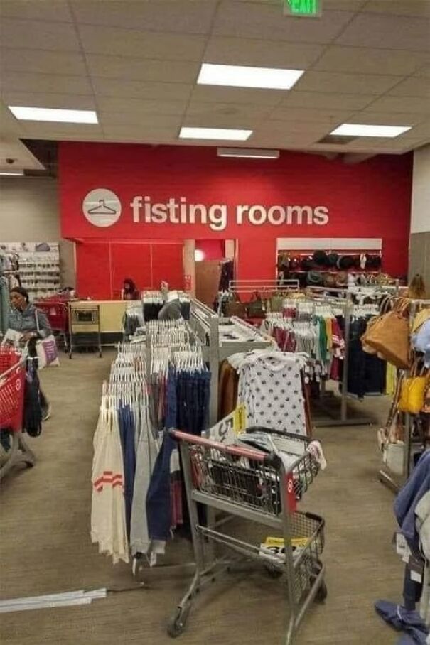 Weird and absurd sign in a store saying "fisting rooms" instead of "fitting rooms" with clothes racks and shopping carts.