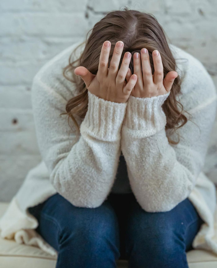 Teen with hands on face, wearing a white sweater and jeans, sitting in distress. Teen with hands on face, wearing a white sweater and jeans, sitting in distress.
