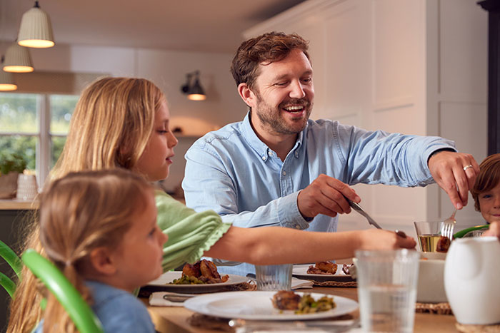 A family enjoying a meal together at home, featuring a man in a blue shirt with children at the table. A family enjoying a meal together at home, featuring a man in a blue shirt with children at the table.