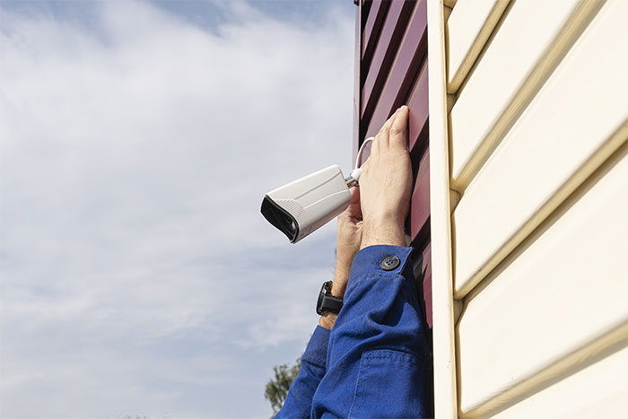 Person adjusting a security camera on the side of a building, wearing a blue sleeve and wristwatch. Person adjusting a security camera on the side of a building, wearing a blue sleeve and wristwatch.