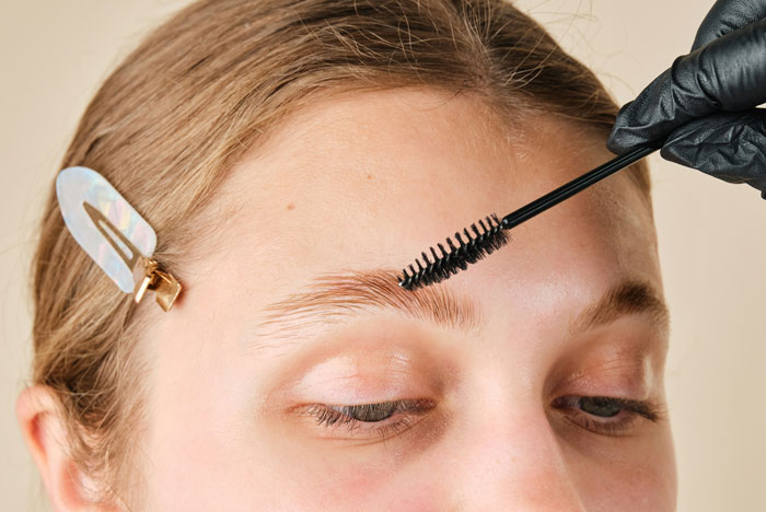 Person receives eyebrow grooming with brush; trends in focus.