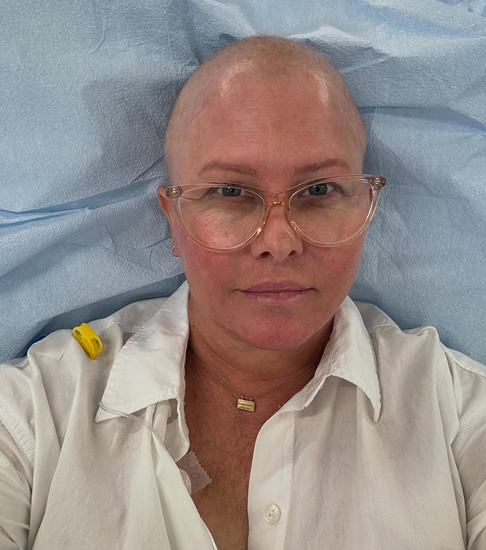 Nicole Eggert wearing glasses and a white shirt, resting on a blue surface, hints of medical setting. Nicole Eggert wearing glasses and a white shirt, resting on a blue surface, hints of medical setting.