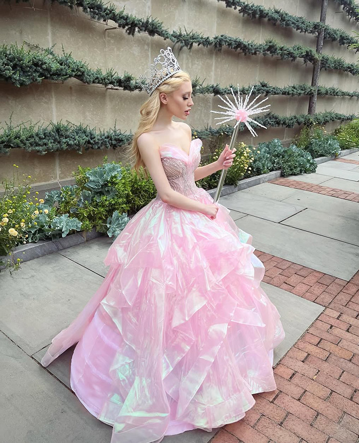 Ariana Grande impersonator Paige Niemann in a pink gown and crown, standing outdoors with a wand. Ariana Grande impersonator Paige Niemann in a pink gown and crown, standing outdoors with a wand.