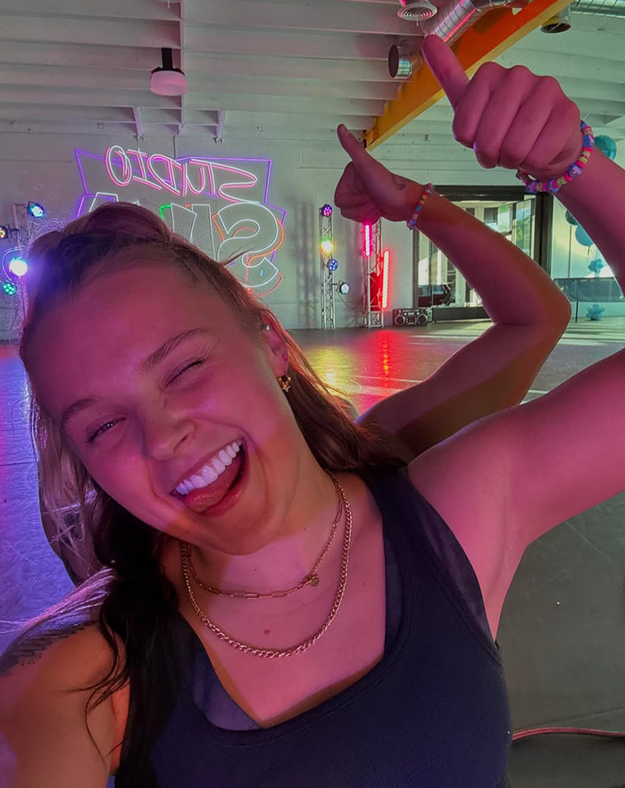 JoJo Siwa smiling and giving thumbs up in a colorful dance studio, related to the celebrity “ignore list” trend. JoJo Siwa smiling and giving thumbs up in a colorful dance studio, related to the celebrity “ignore list” trend.