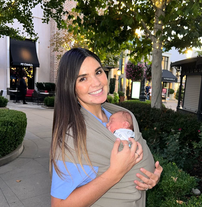 Momfluencer smiling while holding her baby in a sling outdoors. Momfluencer smiling while holding her baby in a sling outdoors.