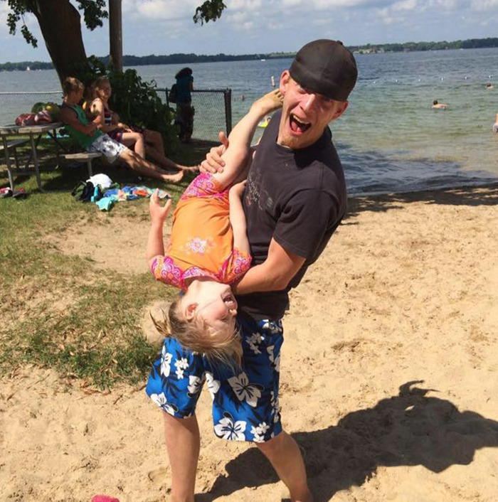 Natalie Rupnow and her father in floral shorts at a lakeside beach, with others relaxing in the background. Natalie Rupnow and her father in floral shorts at a lakeside beach, with others relaxing in the background.