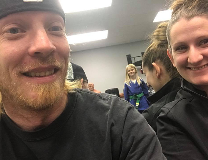 Natalie Rupnow's parents smiling in a room as she poses in the background. Natalie Rupnow's parents smiling in a room as she poses in the background.