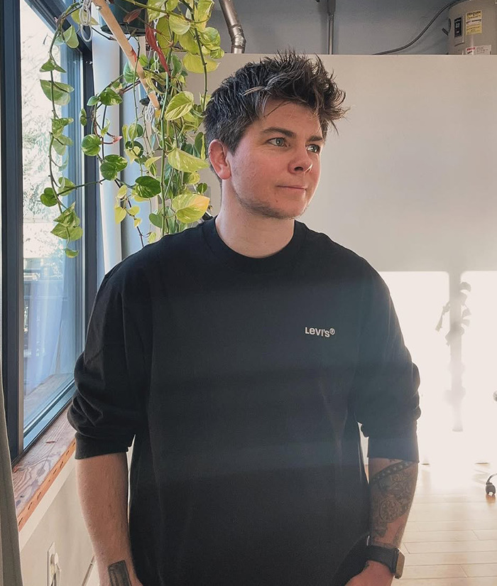 Jules Heron in a salon with short hair, standing near a window. Jules Heron in a salon with short hair, standing near a window.
