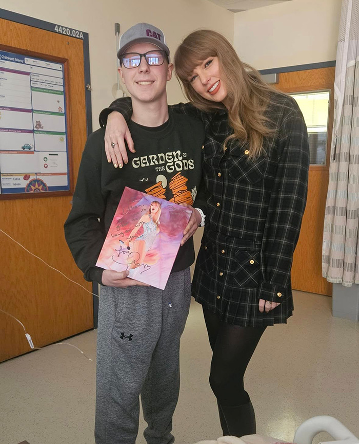 Taylor Swift visits a children's hospital, smiling with a fan holding her album. Taylor Swift visits a children's hospital, smiling with a fan holding her album.