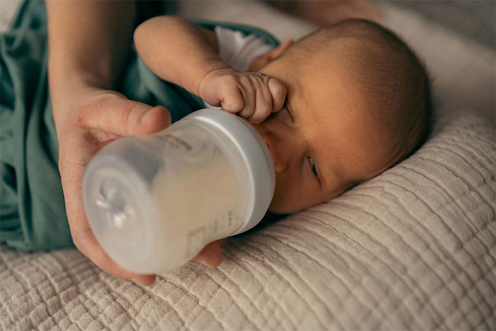 A baby being bottle-fed while lying on a blanket, related to a woman's decision about her mother-in-law seeing the baby. A baby being bottle-fed while lying on a blanket, related to a woman's decision about her mother-in-law seeing the baby.