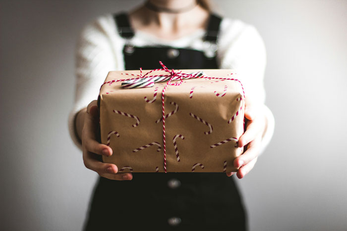 Gift wrapped in brown paper with candy cane design, held out by a person in black overalls. Gift wrapped in brown paper with candy cane design, held out by a person in black overalls.
