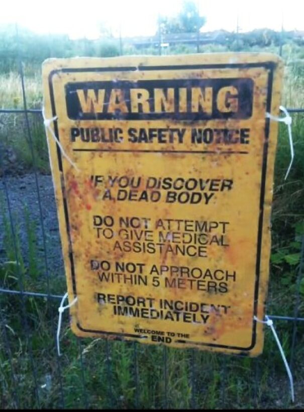 Weird and absurd warning sign about public safety regarding dead bodies, posted on a fence outdoors.