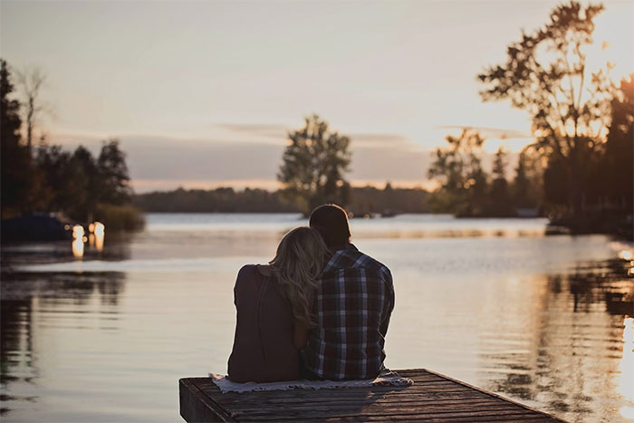 A couple sitting on a dock at sunset by a lake, evoking emotions tied to family and relationship dynamics. A couple sitting on a dock at sunset by a lake, evoking emotions tied to family and relationship dynamics.