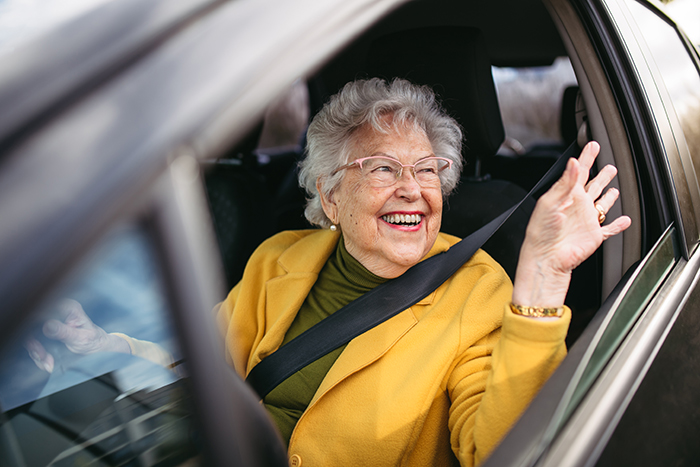 Elderly woman in yellow coat smiling and waving from a car window, representing the unannounced visit theme. Elderly woman in yellow coat smiling and waving from a car window, representing the unannounced visit theme.