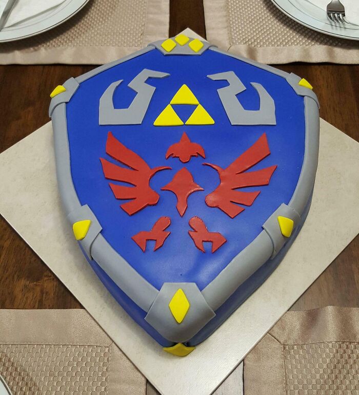 A shield-shaped cake on a table, designed with blue, red, and yellow accents, an amazing mothers-in-law gift idea.
